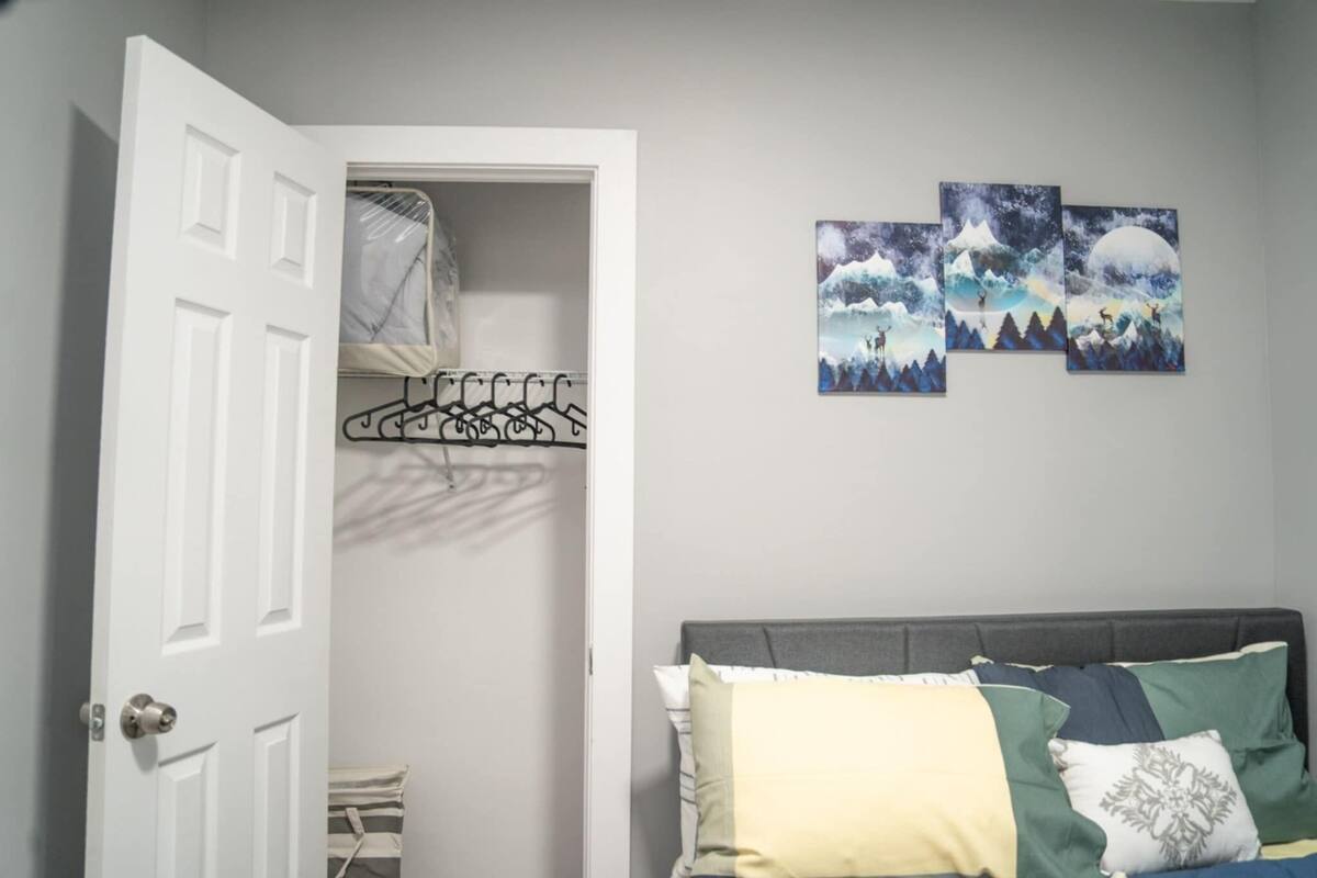 Une chambre à coucher avec un lit, une armoire où sont suspendus des vêtements, et trois tableaux accrochés au mur.