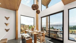 Un espace repas moderne avec une grande table, des chaises en bois et un banc. De grandes fenêtres offrent une vue sur l’extérieur.
