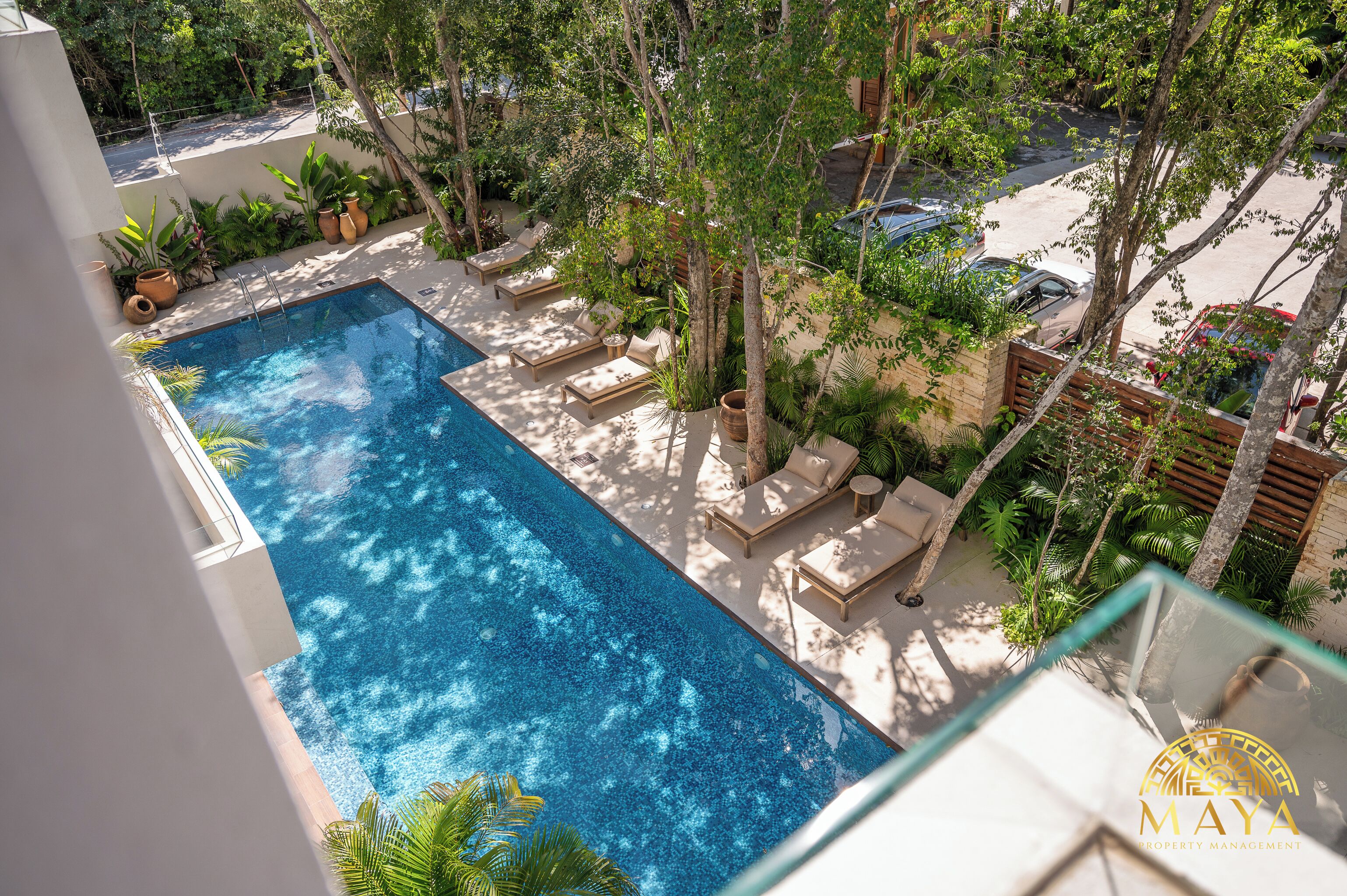 A rooftop pool with lounge chairs and potted plants.
