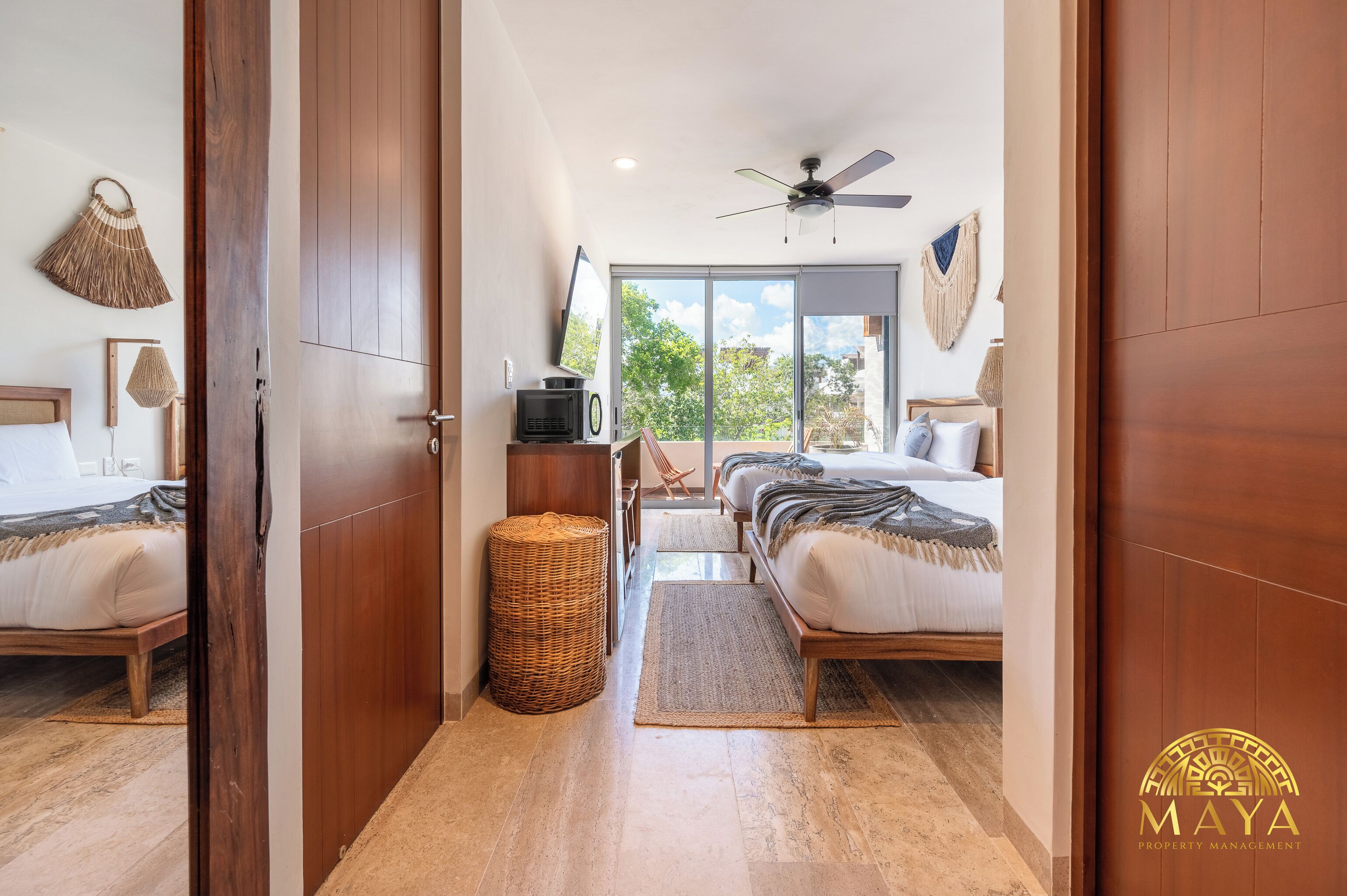 A hotel room with a bed, a TV, a ceiling fan, and a view of the outdoors.
