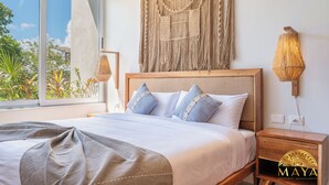 Une chambre avec un lit, une table de chevet, une décoration murale en macramé et une vue sur la verdure à l’extérieur.