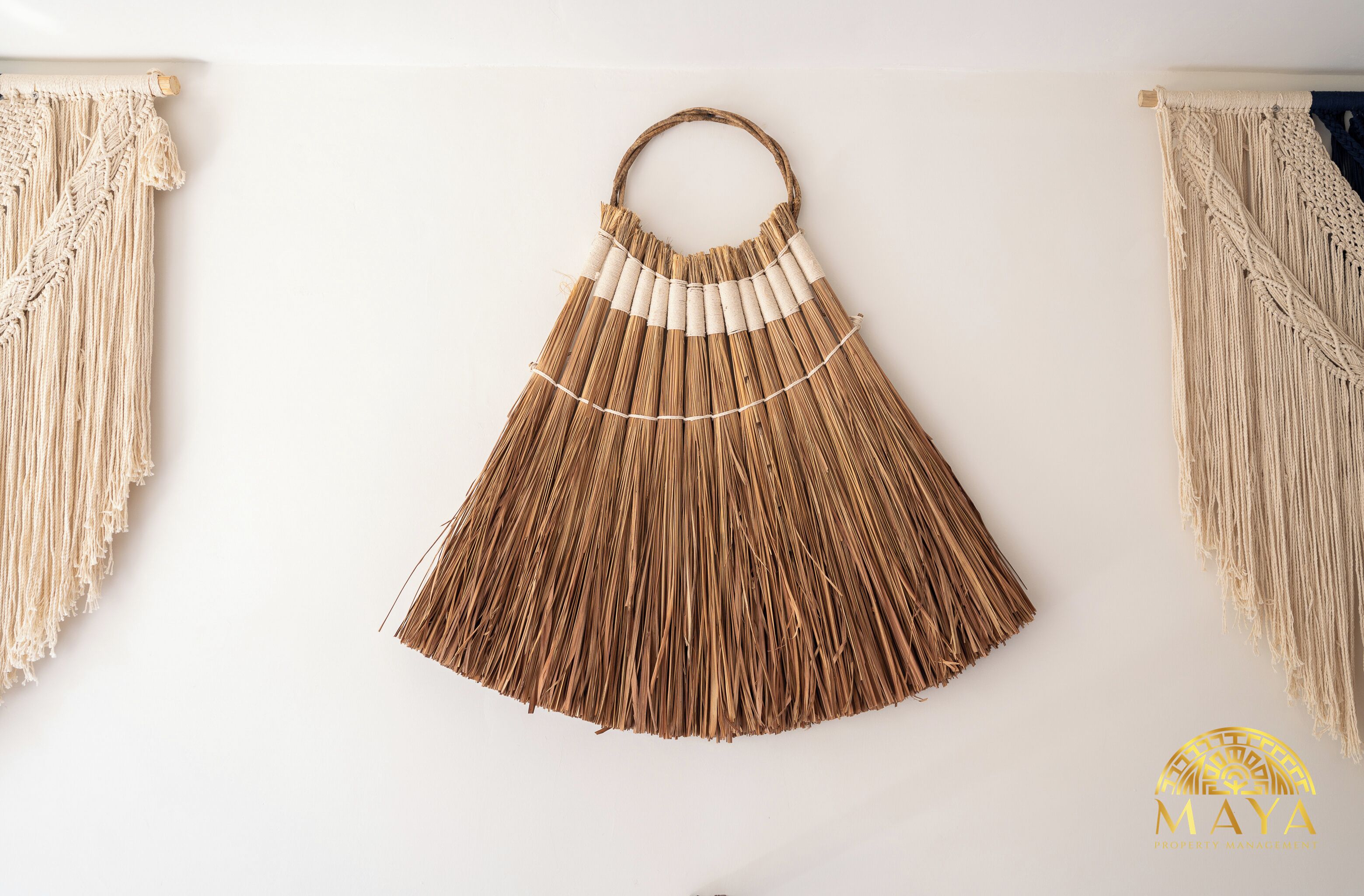 A macrame wall hanging with a circular handle, hanging on a white wall.