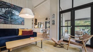A modern living room with a blue sofa, a wooden coffee table, and a rocking chair. There is a large window with a view of the outdoors. - Stunning home in Asnæs with WiFi (Asnæs)