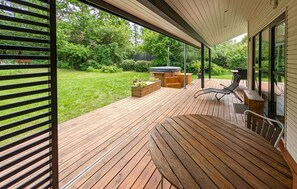 Una terraza de madera con mobiliario exterior, un jacuzzi y vistas a un jardín exuberante.