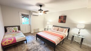 A bedroom with two beds, a ceiling fan, an air conditioning unit, and a window with curtains. - Spacious 2-bedroom, 1 bathroom Basement Apartment near Braves Stadium (Marietta)