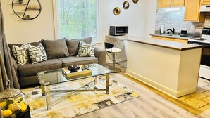 A modern kitchen with a central island, a dining area with a glass table, and a living room with a sofa and decorative pillows. - Spacious 2-bedroom, 1 bathroom Basement Apartment near Braves Stadium (Marietta)