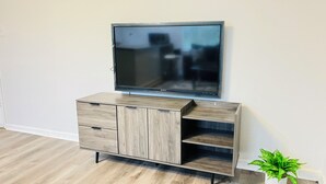 A flat-screen TV on a wooden TV stand with drawers, a potted plant, and a light-colored wooden floor. - Spacious 2-bedroom, 1 bathroom Basement Apartment near Braves Stadium (Marietta)