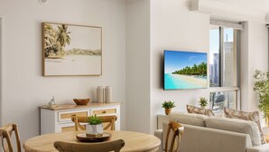 En moderne stue med et rundt træspisebord, en beige sofa og et fladskærms TV monteret på væggen.