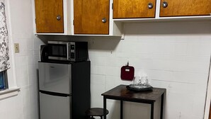 A compact kitchen with a refrigerator, microwave, and a small table with stools.