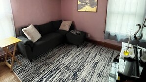 A living room with a ceiling fan, a black sofa, a patterned rug, a small wooden table, and a window with blinds.