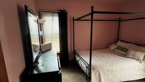 A bedroom with a four-poster bed, a dresser with a mirror, and a window with blinds.