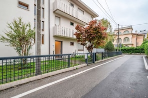 Um edifício residencial com vários andares, varandas, entrada com portão e um gramado bem cuidado.