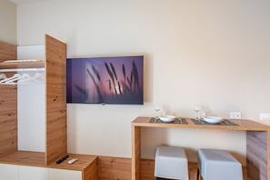 Quarto moderno com armário de madeira, televisão montada, mesa de jantar com cadeiras e um banco.