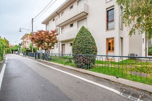 Une rue résidentielle avec un immeuble blanc, une haie verte et une clôture en métal.