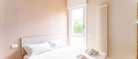 Una habitación de hotel moderna con una cama grande, una ventana con persianas, un radiador y vistas a zonas verdes.