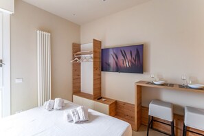 Une chambre d’hôtel moderne  équipée d’un lit, d’une télévision, d’un bureau en bois avec un lavabo et d’un miroir.