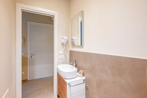 Casa de banho com lavatório branco, espelho e secador de cabelo na parede.