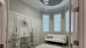 Ein geräumiger Raum mit einem großen, weißen, flauschigen Teppich, einer weißen Couch, einer Chandelierleuchtre und einer Vitrine mit dekorativen Gegenständen.