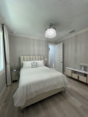 Een slaapkamer met een groot bed, een nachtkastje, een kaptafel, een dressoir, een kroonluchter en een deur.