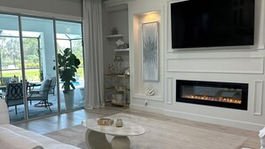 Ein modernes Wohnzimmer mit großem Fernseher, Kamin und weißen Möbeln.
