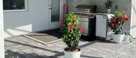 A covered patio area with a grill, potted plants, and a ceiling fan.