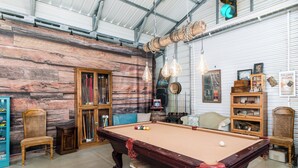 Una mesa de billar en una sala con decoración rústica, que incluye un muro de madera y un techo con vigas a la vista.