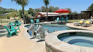 Zona de piscina con un jacuzzi circular, sillas de descanso y estatuas decorativas de cebra.
