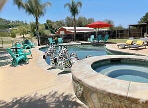 Zona de piscina con un jacuzzi circular, sillas de descanso y estatuas decorativas de cebra.