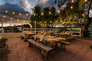 An outdoor dining area with wooden tables and benches, string lights, and a rustic fence. - 7BR Ranch Estate • Pool • Hot Tub • Game Room • Wineries • Farm Experience (Ramona)