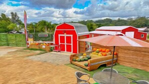 Una granja con un granero rojo, un puesto de verduras y mesas al aire libre.