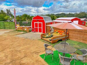 Une ferme avec une grange rouge, un stand de vente de légumes et des tables à l’extérieur.