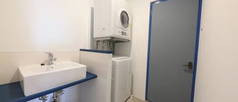 A compact bathroom with a white sink, a built-in washing machine, and a door with a blue frame.