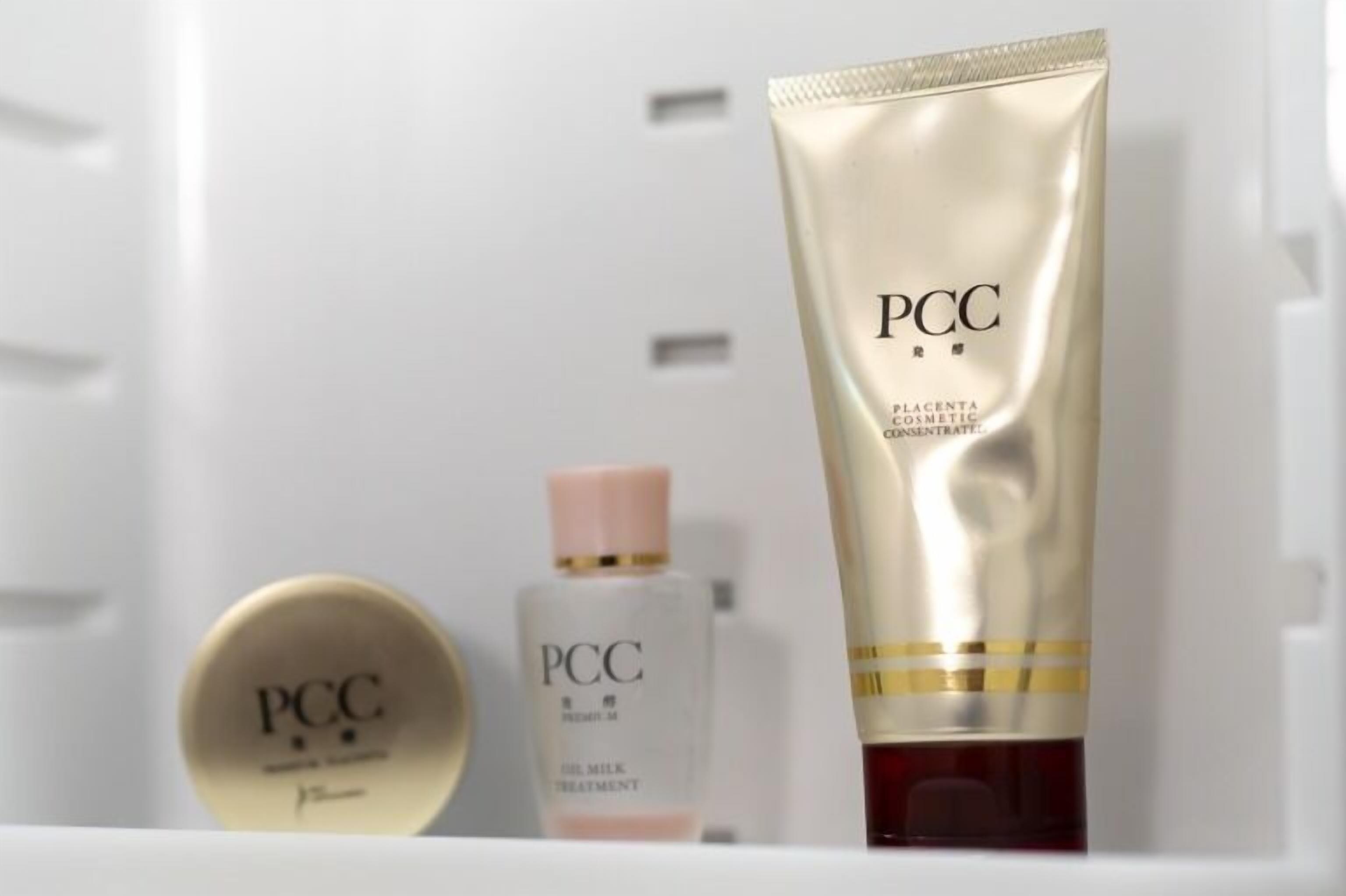 A bathroom with a white sink, a gold PCC skincare product, and a white PCC oil milk treatment bottle.