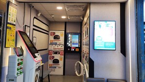 A self-service laundry facility with a digital screen, a dryer, and a seating area. - KK Hotel  (Kowloon)