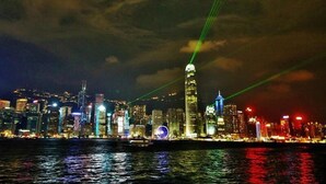 A nighttime cityscape with illuminated buildings and a river in the foreground. - KK Hotel  (Kowloon)