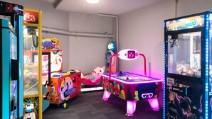 Una habitación con juegos de arcade, una máquina de premios y una mesa con luz de neón.