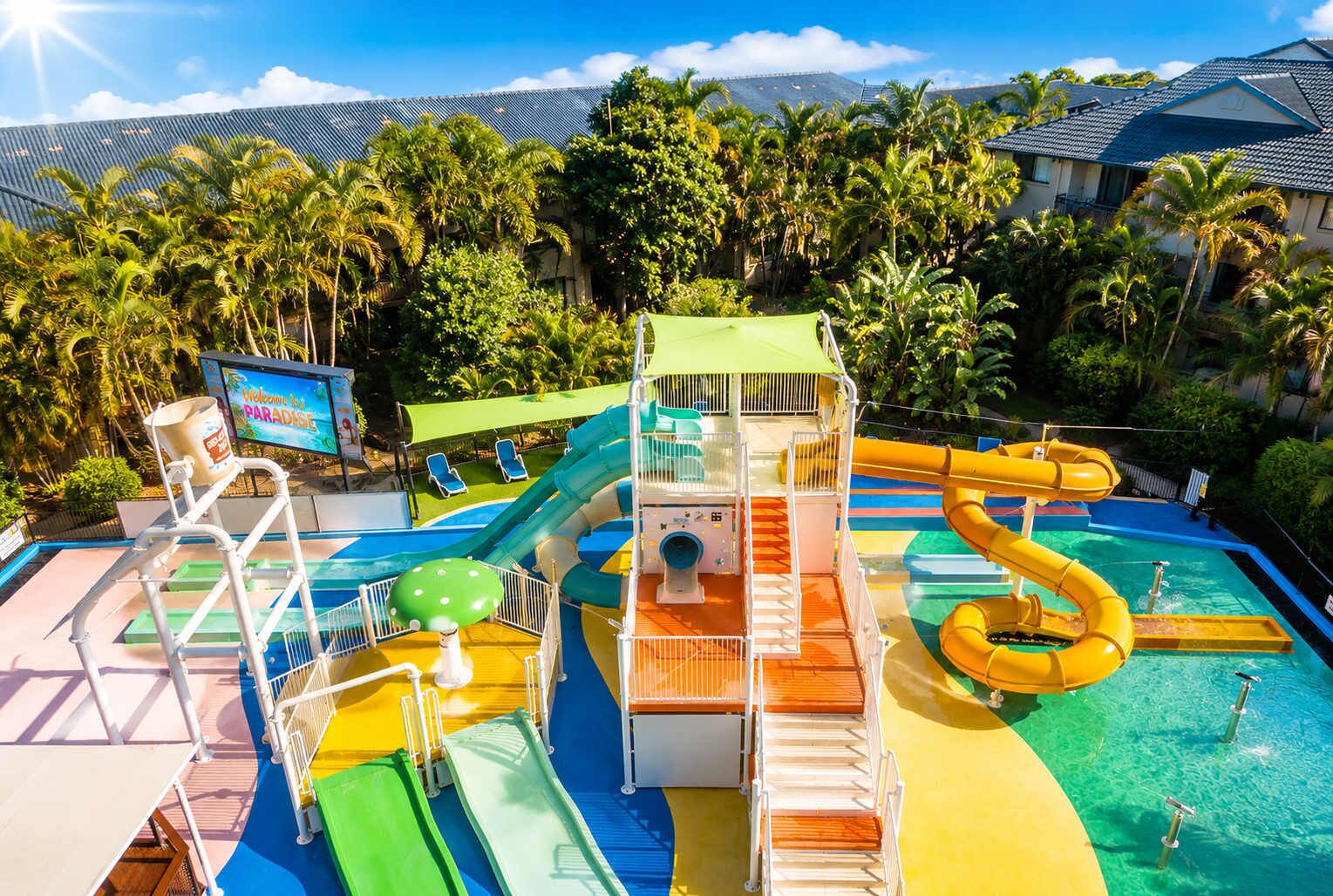 A water park with multiple slides and pools, surrounded by palm trees and a clear sky.