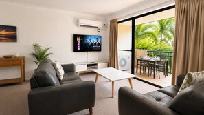 Uma sala de estar moderna com televisão de tela plana, sofás de couro, uma mesa de centro e uma porta de vidro deslizante que dá para uma área de refeições ao ar livre.