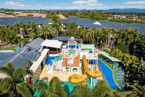 Un parc aquatique avec des toboggans et des piscines, entouré de palmiers et de maisons.