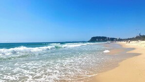 Une plage avec des vagues, un ciel dégagé et des bâtiments en arrière-plan.