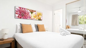 Habitación de hotel con una cama grande, una mesita de noche con lámpara, un cuadro de flores, un espejo y una ventana con cortinas.