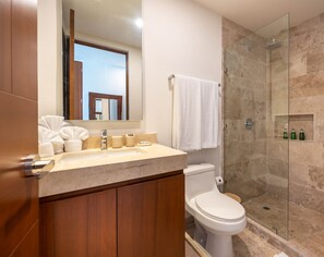 Un baño moderno con lavamanos de mármol, muebles de madera, inodoro y ducha con cerramiento de vidrio.