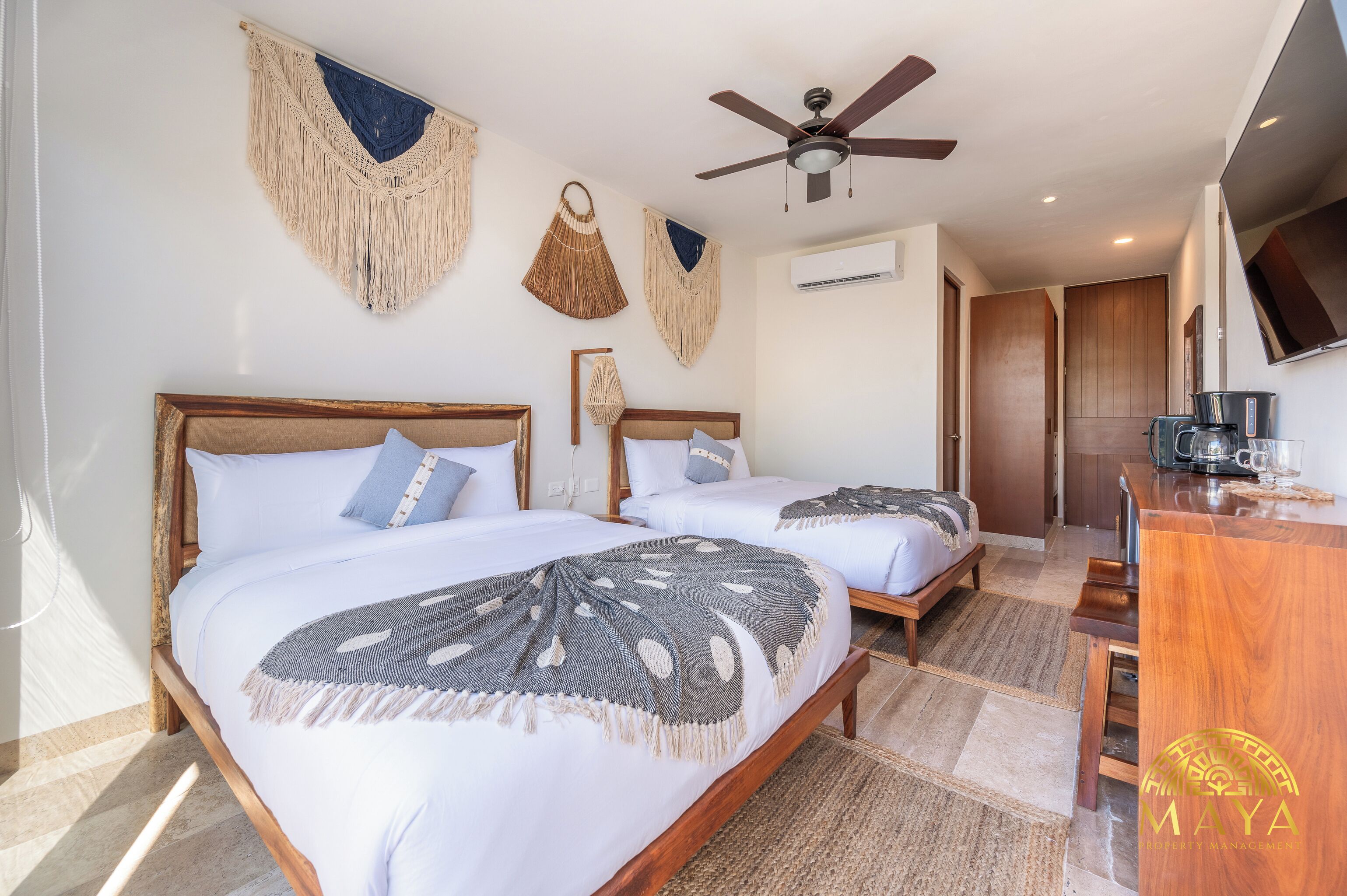A hotel room with two beds, a ceiling fan, a coffee maker, and a TV.