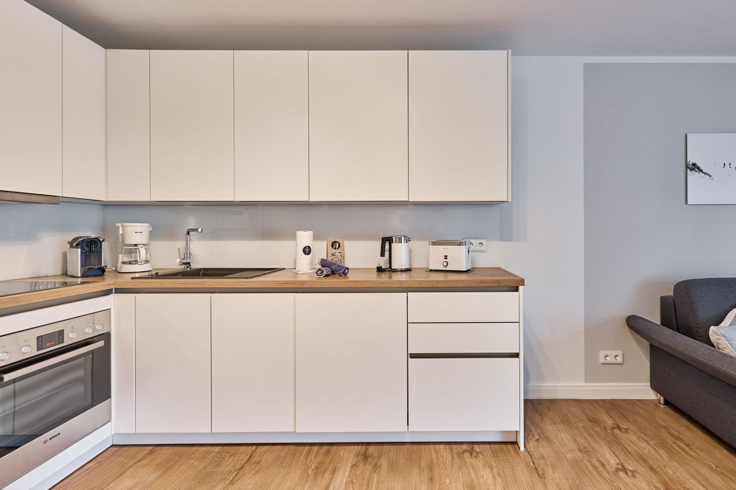 Een moderne keuken met witte kasten, een houten aanrecht, een Bosch oven, een koffiezetapparaat en een broodrooster.