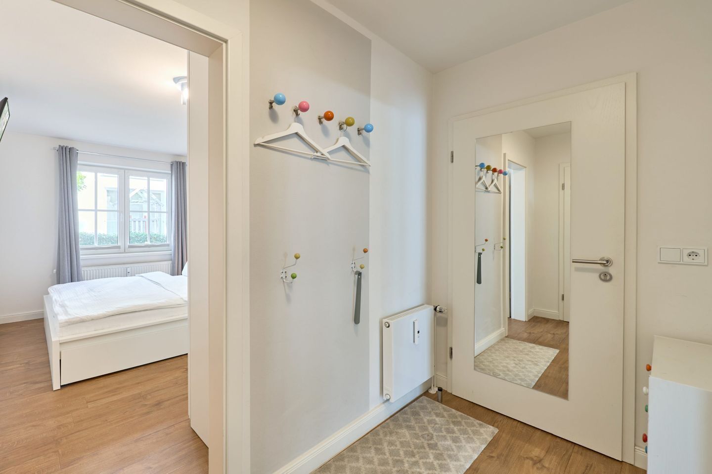A modern bedroom with a bed, a radiator, a mirror, and a door leading to another room.