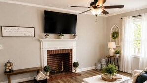A living room with a fireplace, a television, a ceiling fan, and a cozy seating area.