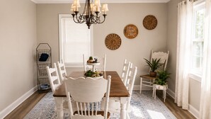 A dining room with a wooden table, white chairs, a chandelier, and decorative plates on the wall.
