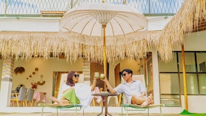 A poolside area with a table and chairs, a large umbrella, and a thatched roof structure. - Dsvarga Glamping (Depok)