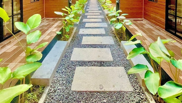 A corridor with a thatched roof, wooden walls, and a pebble path lined with plants. - Dsvarga Glamping (Depok)