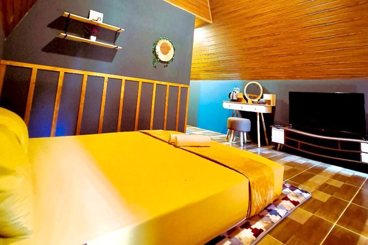 Een moderne slaapkamer met een groot bed, houten plafond, een klein bureau en een televisie.